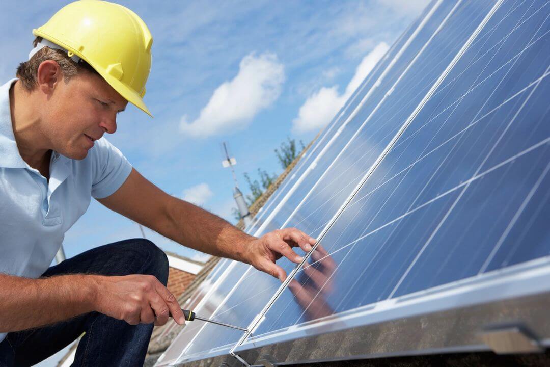 A man in yellow hard hat working on solar panel.