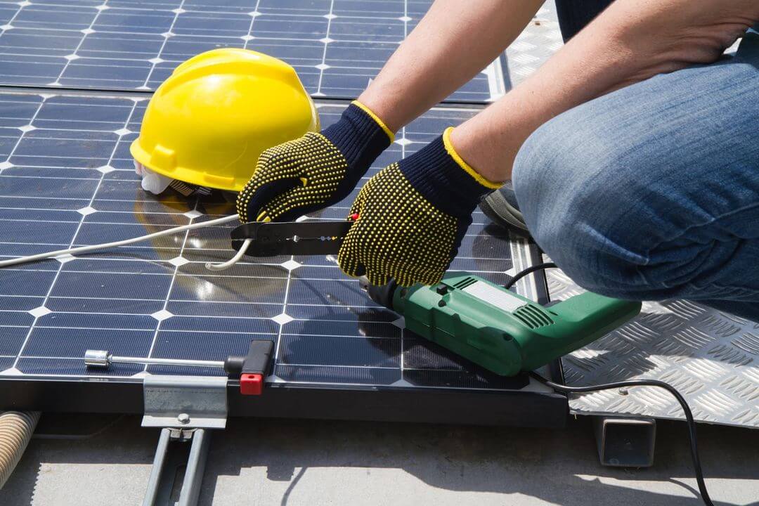 A person with gloves and hard hat working on solar panel.