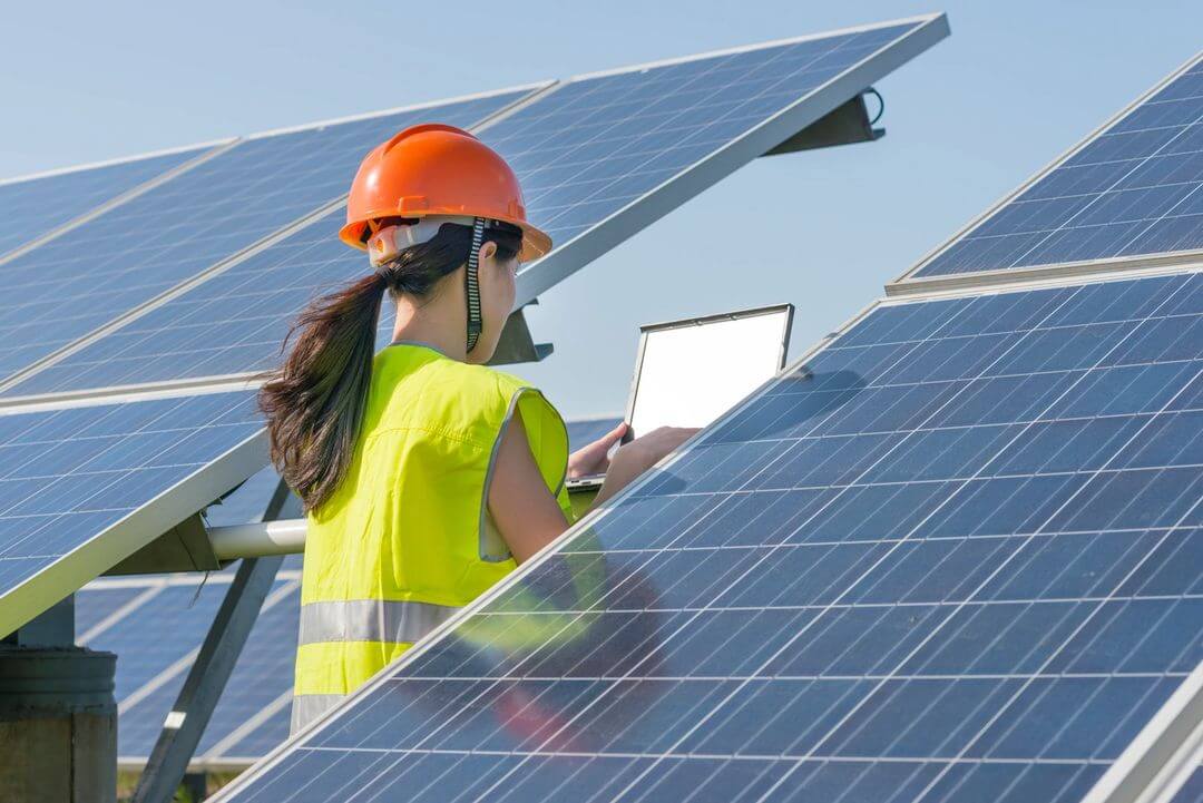 A woman in an orange helmet is working on some solar panels.